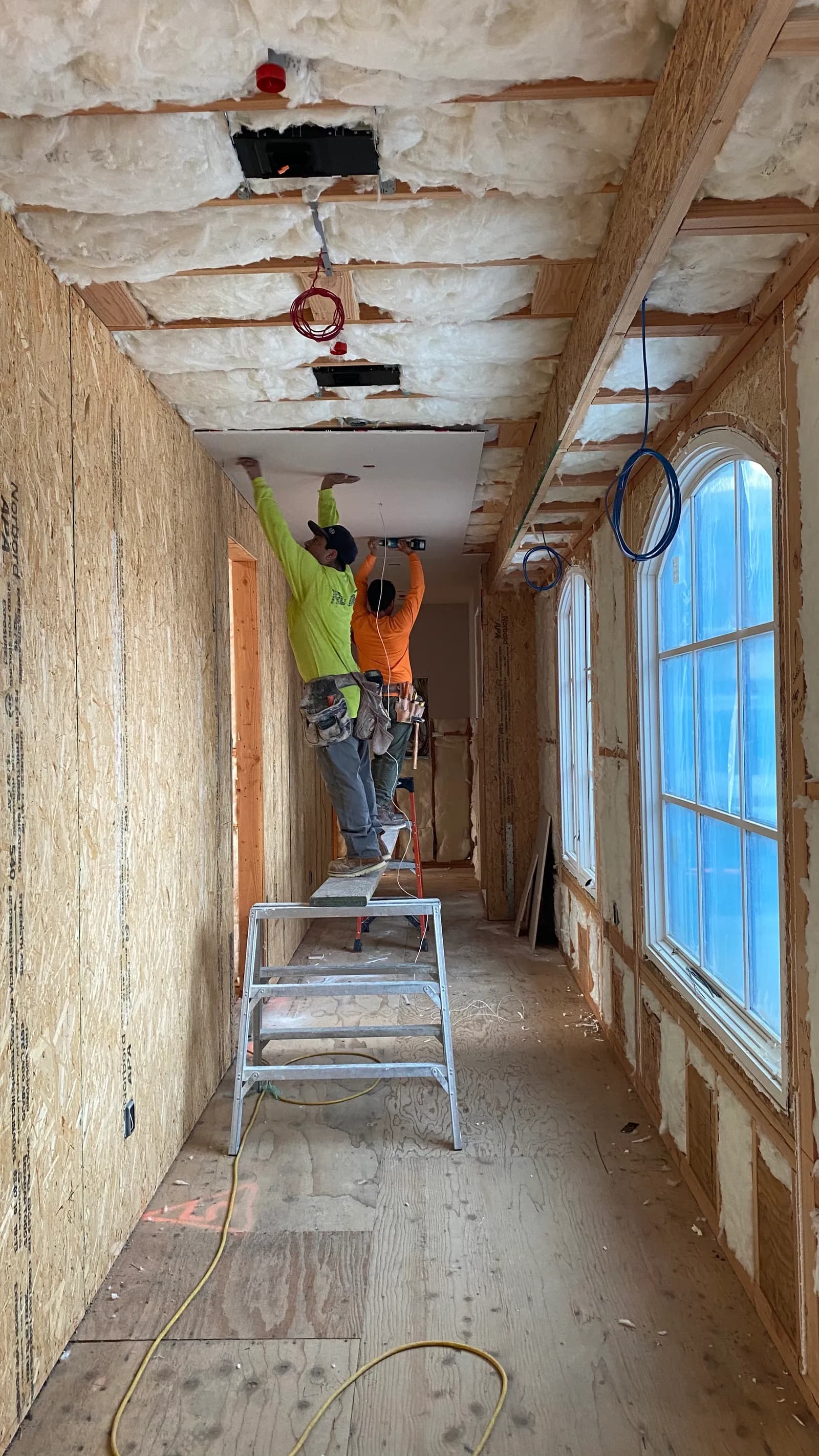 A long corridor in framing and insulation, daylight entering from arched openings down one side.